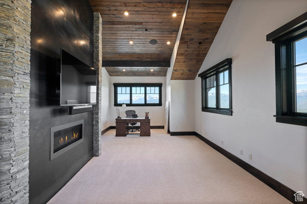 Unfurnished living room with wood ceiling, light colored carpet, plenty of natural light, vaulted ceiling, and a glass covered fireplace