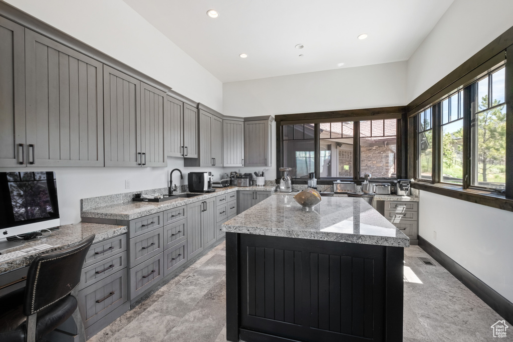 Kitchen with gray cabinets, a sink, light stone countertops, a center island, and recessed lighting