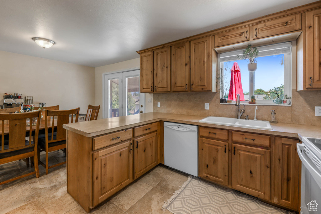 Kitchen featuring white appliances, a sink, a peninsula, backsplash, and light countertops
