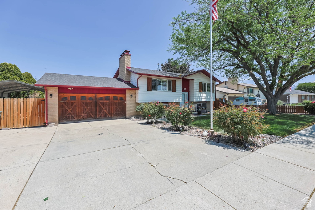Raised ranch with brick siding, an attached garage, driveway, and a chimney