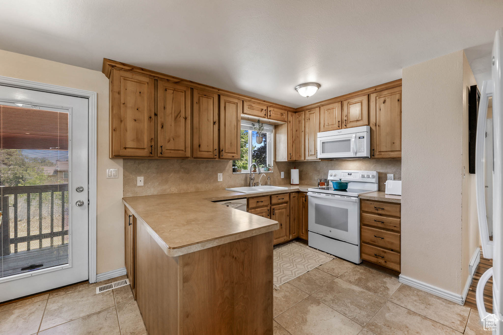Kitchen featuring white appliances, a sink, a peninsula, backsplash, and light countertops