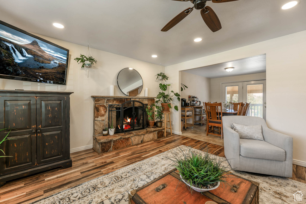 Living room with wood finished floors, a ceiling fan, a stone fireplace, baseboards, and french doors