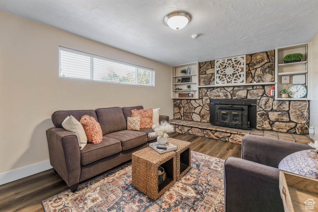 Living room with wood finished floors, baseboards, built in features, and a stone fireplace