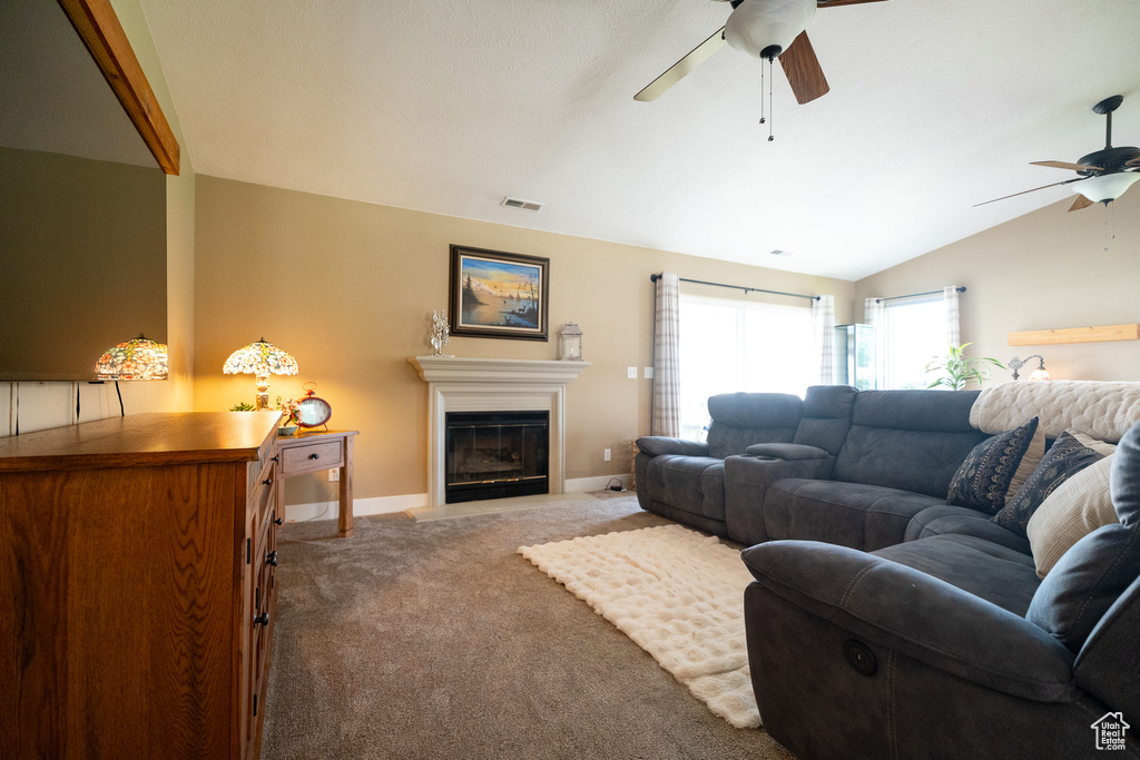Carpeted living area featuring a ceiling fan, vaulted ceiling, baseboards, and a glass covered fireplace
