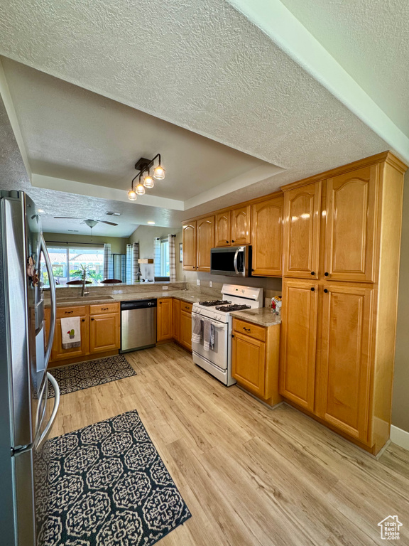 Kitchen with stainless steel appliances, a raised ceiling, a textured ceiling, light wood-type flooring, and a sink