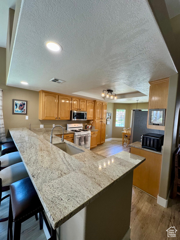 Kitchen featuring white gas range oven, stainless steel microwave, light wood-style flooring, a sink, and a textured ceiling