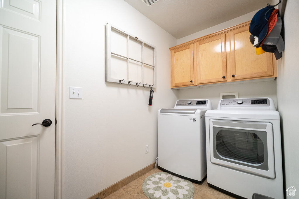 Washroom featuring cabinet space, washer and clothes dryer, baseboards, and light tile patterned flooring