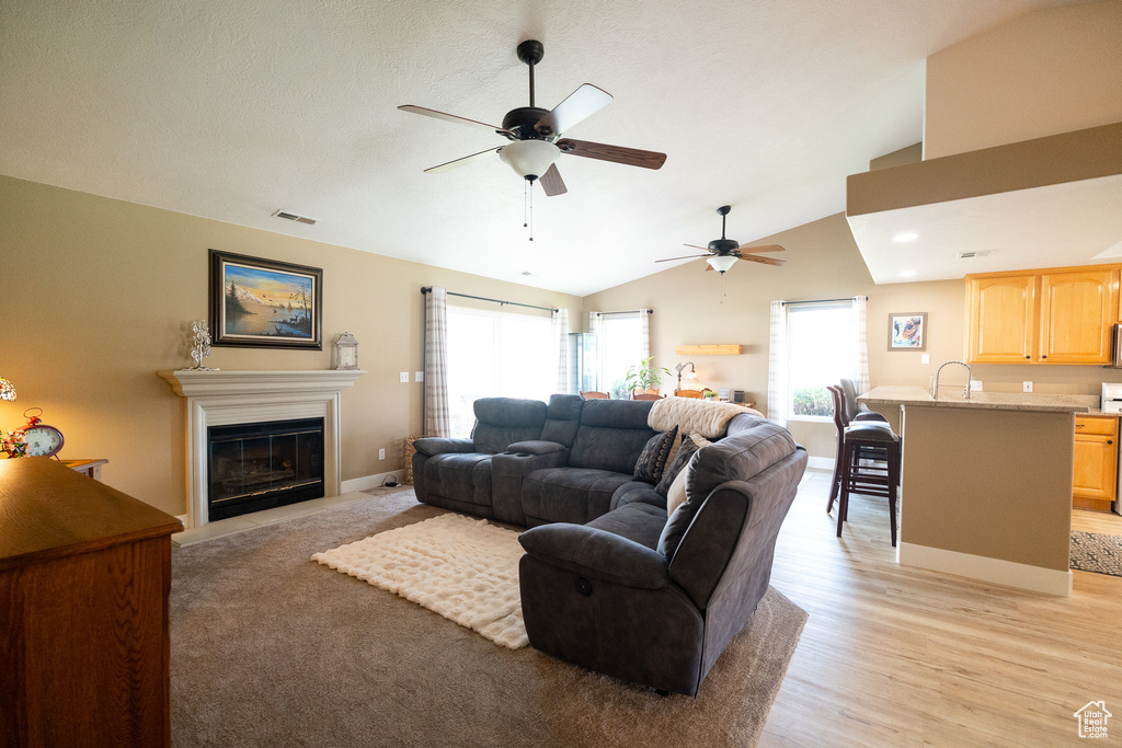 Living room with ceiling fan, lofted ceiling, a fireplace with flush hearth, light wood-style flooring, and baseboards