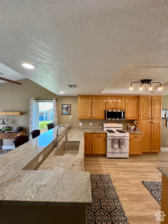 Kitchen featuring white range with gas cooktop, a sink, stainless steel microwave, a textured ceiling, and light wood-type flooring