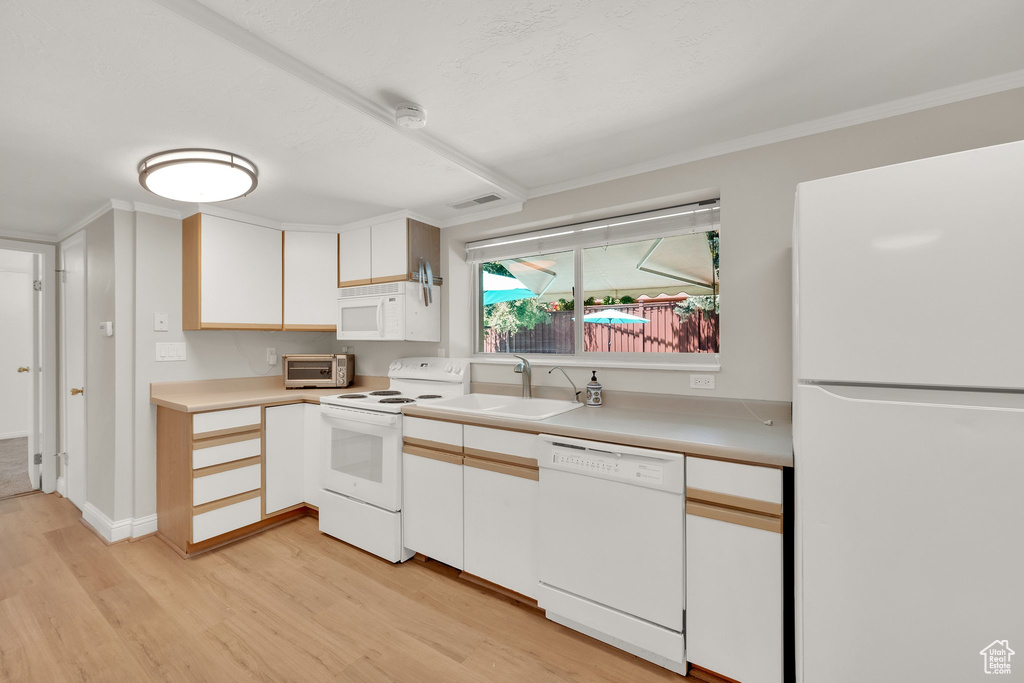 Kitchen featuring white appliances, a sink, light wood finished floors, light countertops, and crown molding