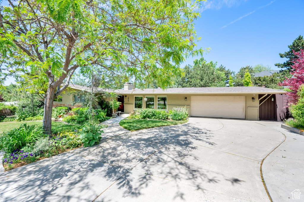 Ranch-style home featuring driveway, an attached garage, a chimney, and stucco siding