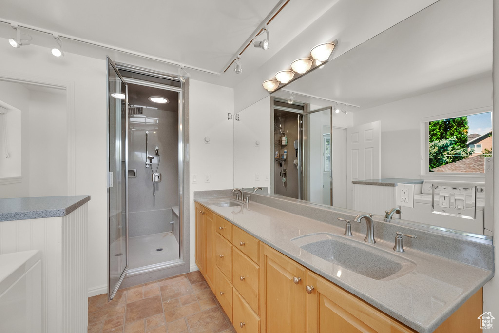 Full bath featuring track lighting, double vanity, a shower stall, baseboards, and stone finish flooring