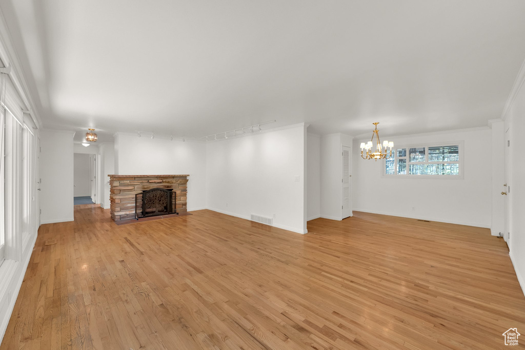 Unfurnished living room with a chandelier, a stone fireplace, light wood finished floors, and baseboards