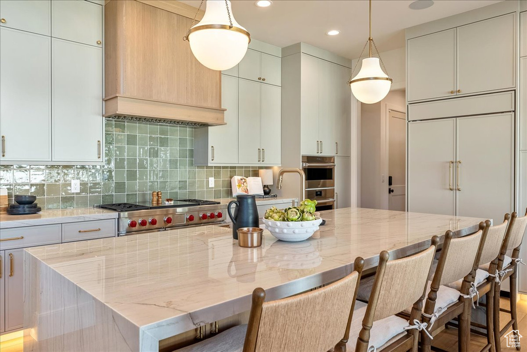 Kitchen featuring appliances with stainless steel finishes, light stone countertops, tasteful backsplash, premium range hood, and a center island