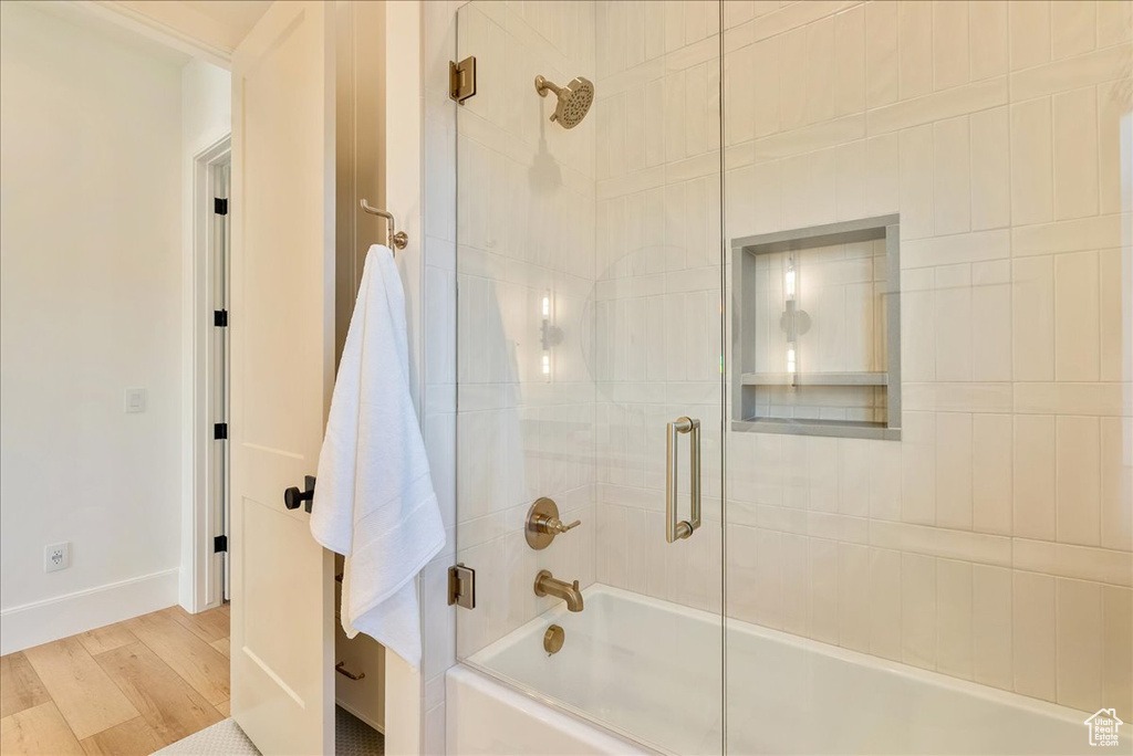 Bathroom with enclosed tub / shower combo, wood finished floors, and baseboards