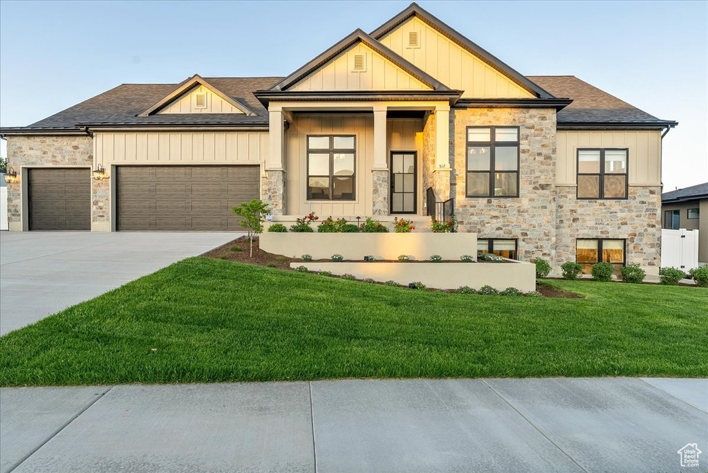 View of front facade featuring stone siding, a front lawn, an attached garage, concrete driveway, and board and batten siding