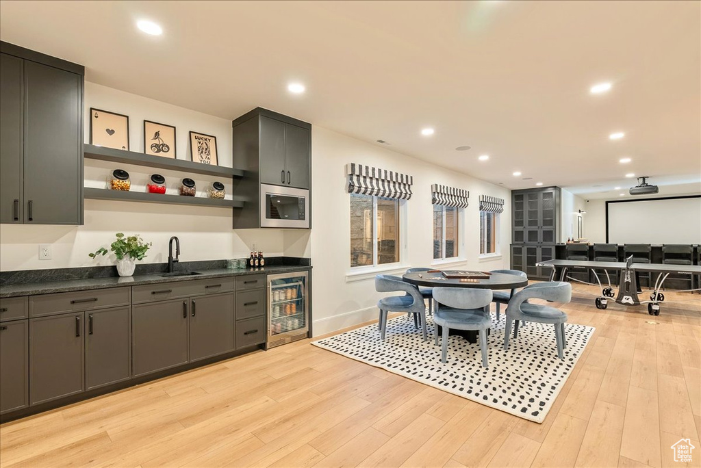 Kitchen with beverage cooler, stainless steel microwave, open shelves, a sink, and dark countertops
