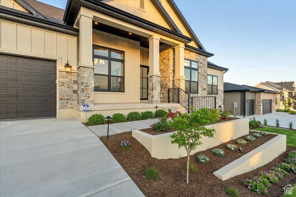 View of front of home with stone siding, board and batten siding, a garage, driveway, and a porch