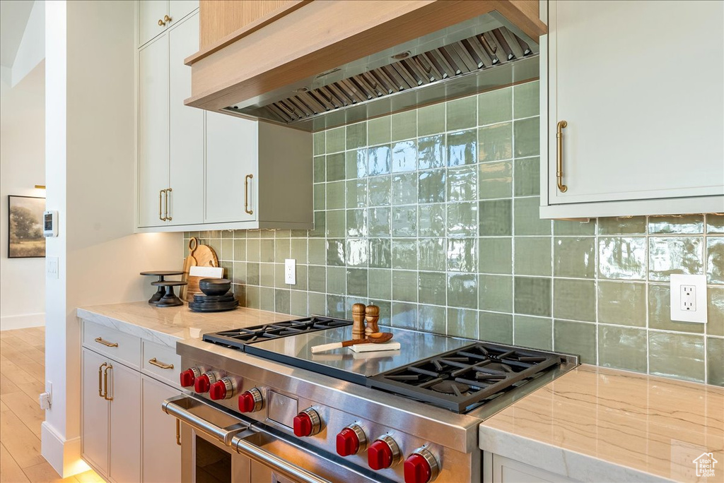 Kitchen with premium range hood, high end range, decorative backsplash, and light stone countertops