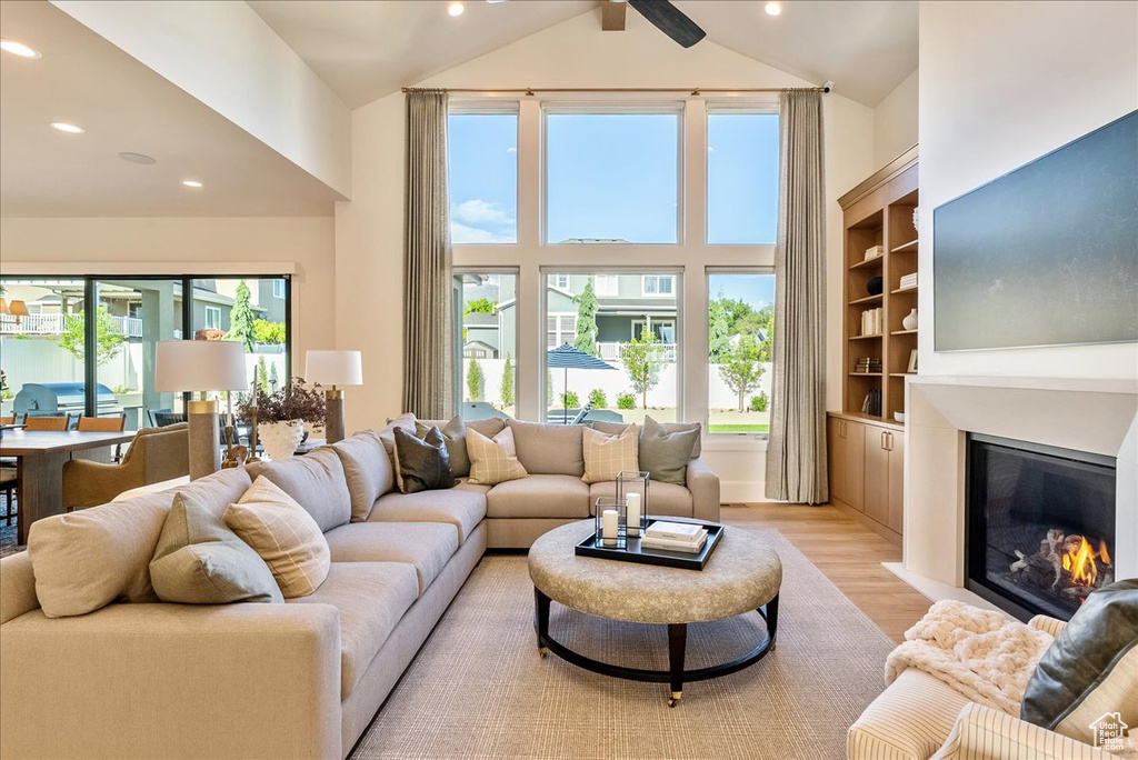 Living room with high vaulted ceiling, light wood-style floors, a glass covered fireplace, and recessed lighting