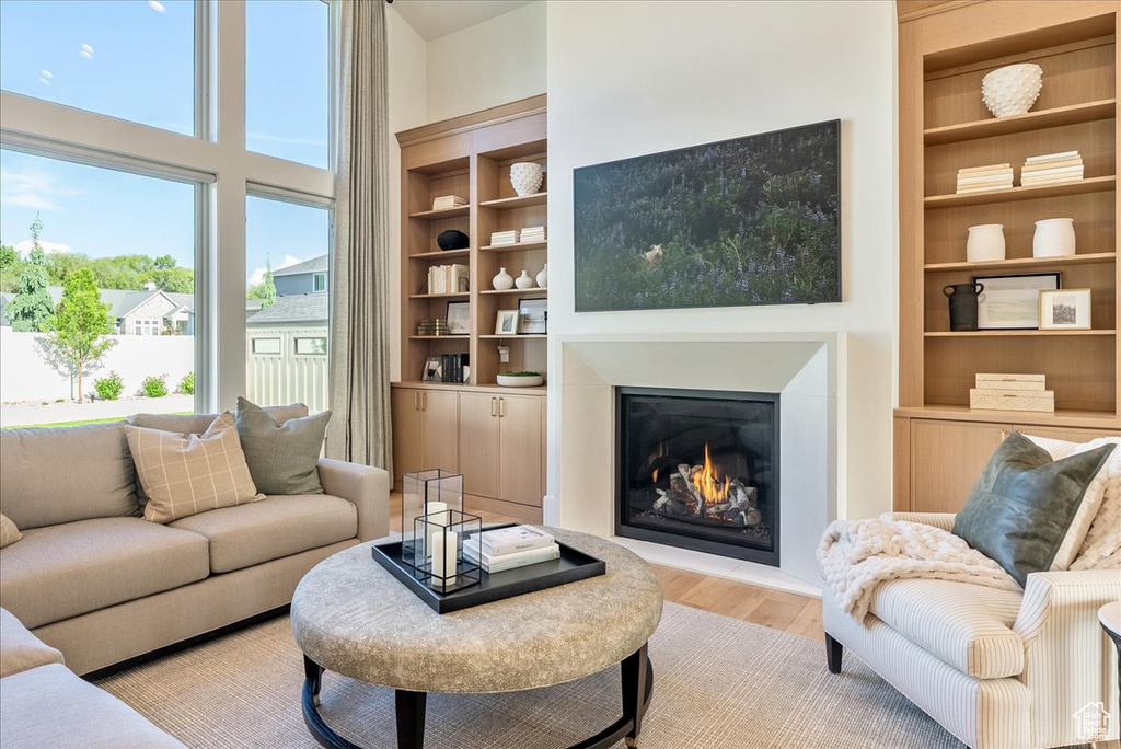 Living room featuring light wood-type flooring, a warm lit fireplace, and built in shelves