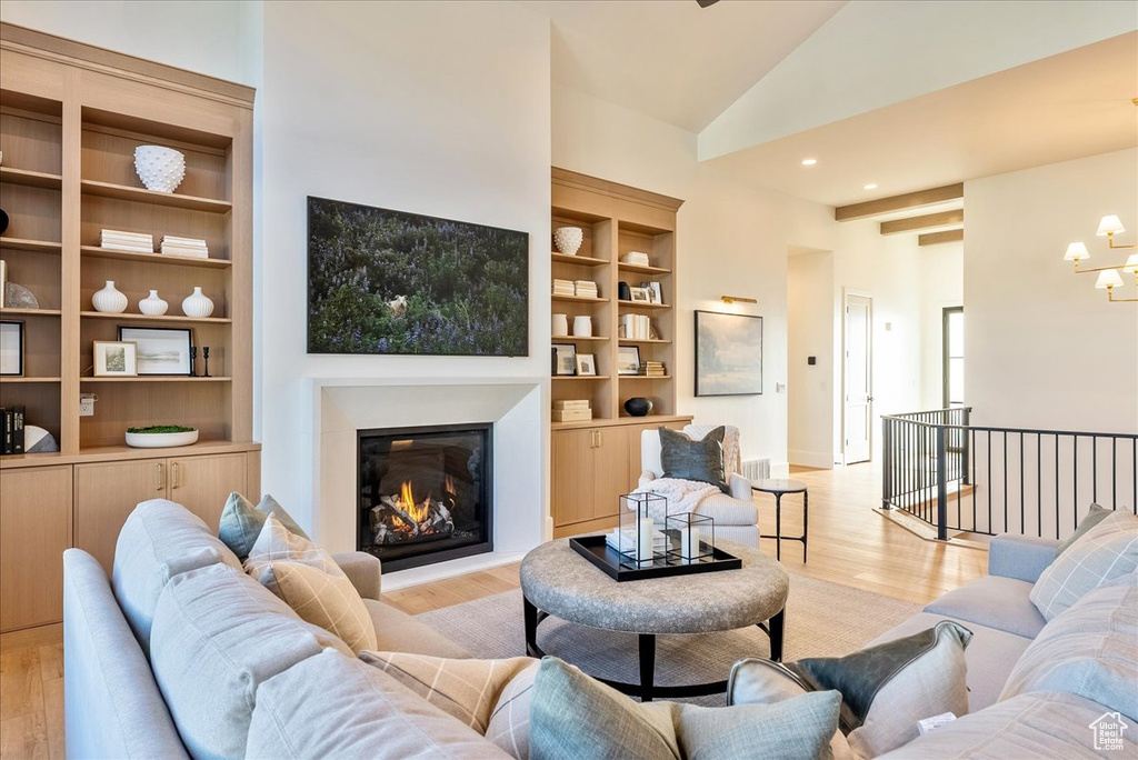Living area featuring light wood-type flooring, a glass covered fireplace, a chandelier, built in shelves, and high vaulted ceiling