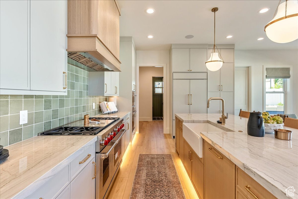 Kitchen with a sink, double oven range, custom range hood, backsplash, and light stone countertops