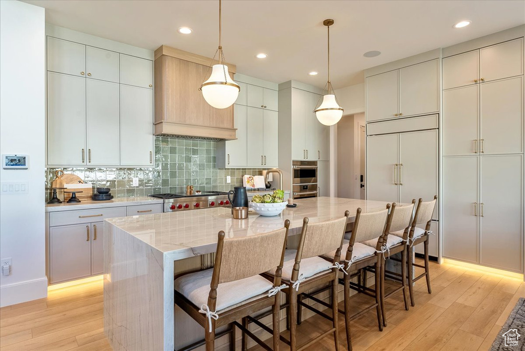 Kitchen featuring light wood finished floors, stove, decorative backsplash, an island with sink, and recessed lighting