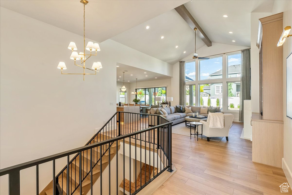 Stairs with beamed ceiling, high vaulted ceiling, healthy amount of natural light, wood finished floors, and a chandelier