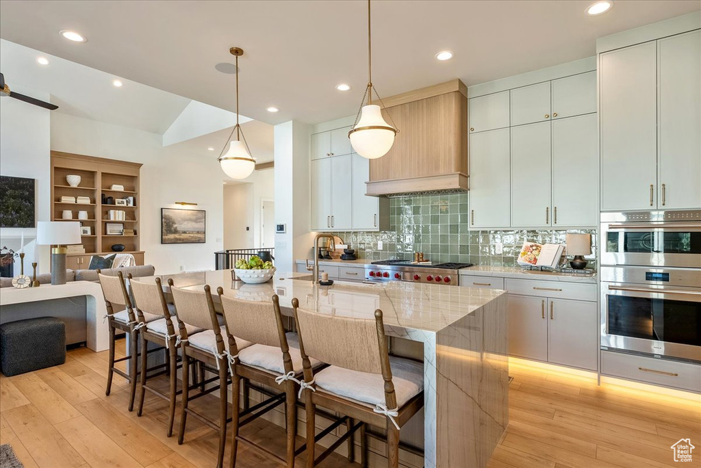 Kitchen with stainless steel appliances, a kitchen island with sink, a kitchen breakfast bar, light wood finished floors, and backsplash
