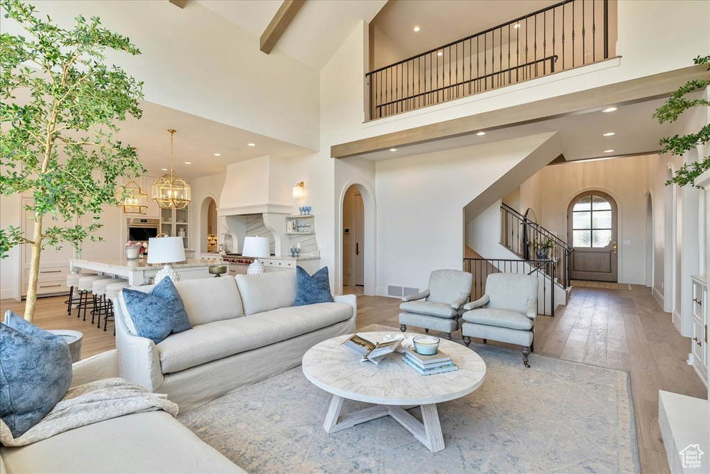 Living room with arched walkways, stairway, light wood-style flooring, a towering ceiling, and a chandelier