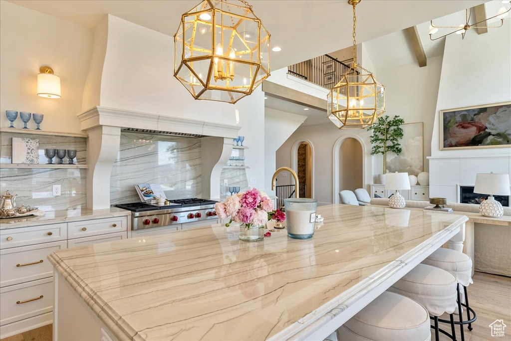 Kitchen featuring a chandelier, a high ceiling, light stone counters, white cabinets, and decorative backsplash