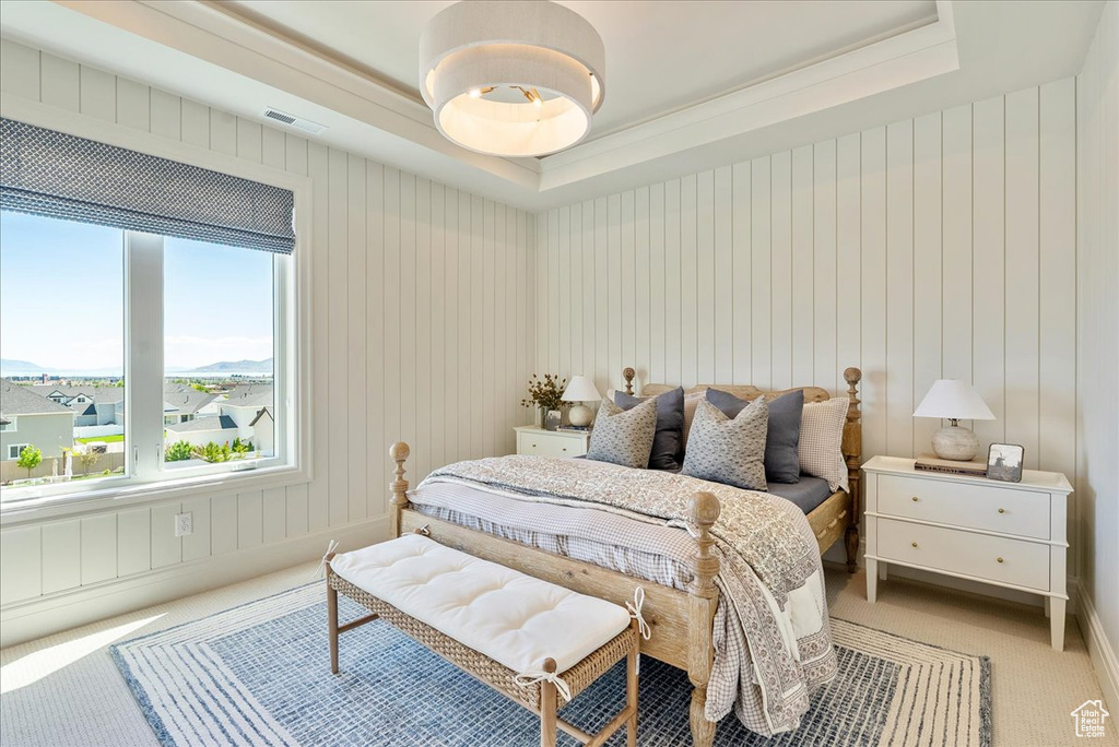 Bedroom with a raised ceiling, light carpet, and ornamental molding