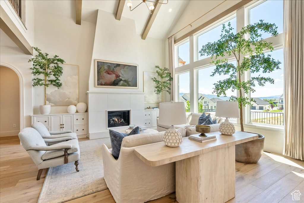 Living area featuring high vaulted ceiling, light wood-style flooring, plenty of natural light, arched walkways, and beam ceiling