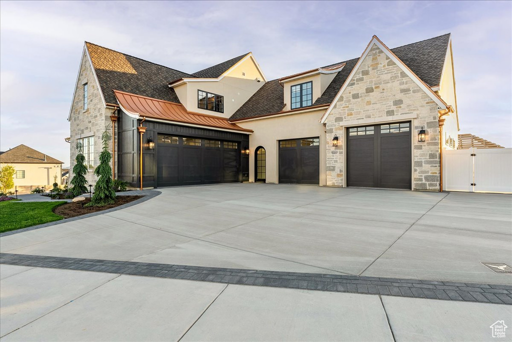 View of front of home with stone siding, a garage, a standing seam roof, driveway, and stucco siding