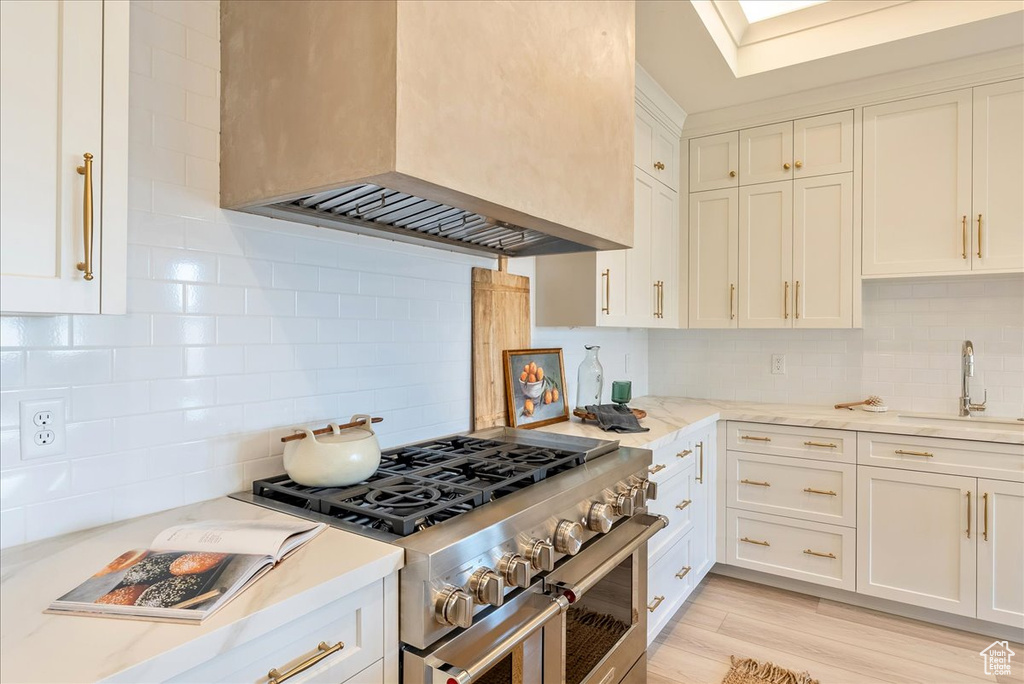 Kitchen featuring double oven range, a sink, premium range hood, decorative backsplash, and white cabinets