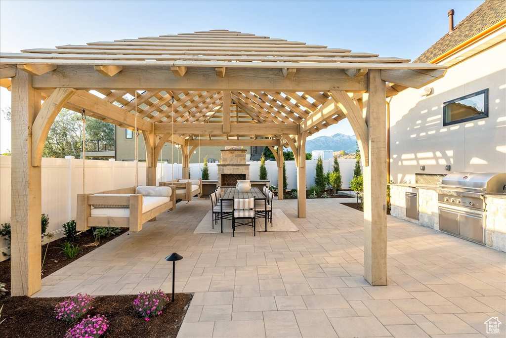 Fenced backyard with an outdoor stone fireplace, a gazebo, a patio, outdoor dining space, and a mountain view
