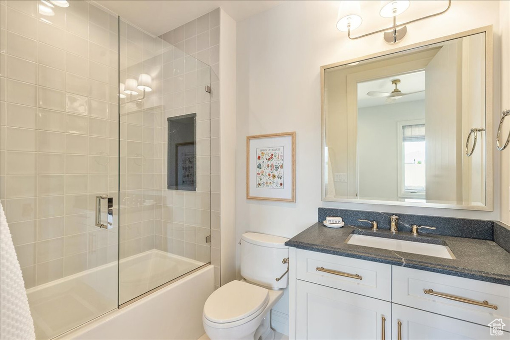 Bathroom with toilet, vanity, combined bath / shower with glass door, and ceiling fan