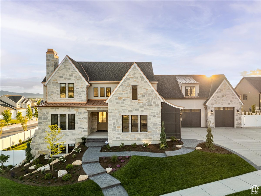 View of front of house featuring a standing seam roof, stone siding, a chimney, concrete driveway, and covered porch