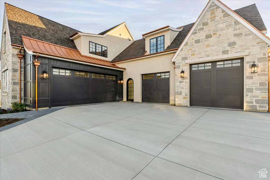 View of front of home featuring stone siding, stucco siding, driveway, a garage, and a standing seam roof