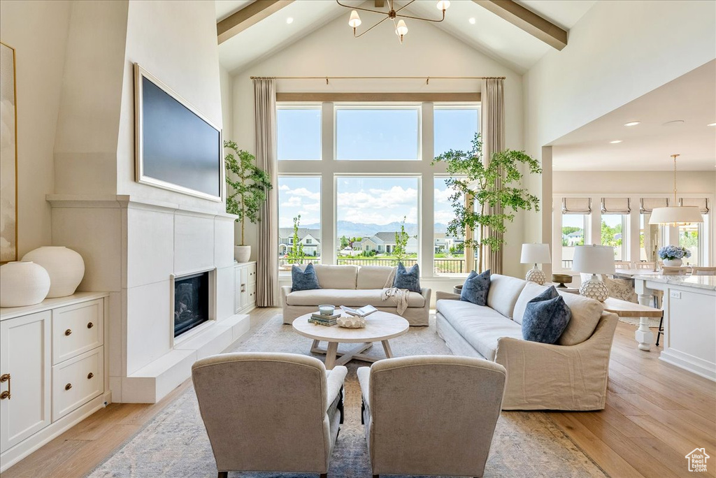 Living area with high vaulted ceiling, light wood-style floors, beam ceiling, a glass covered fireplace, and recessed lighting