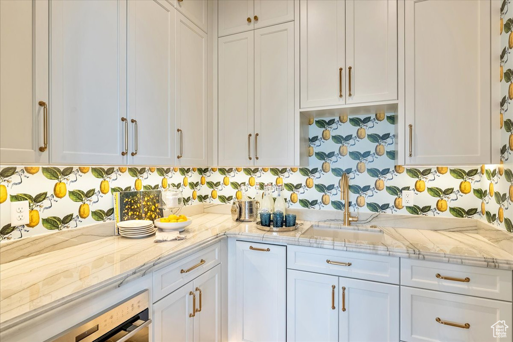 Kitchen with a sink, white cabinetry, and light stone countertops