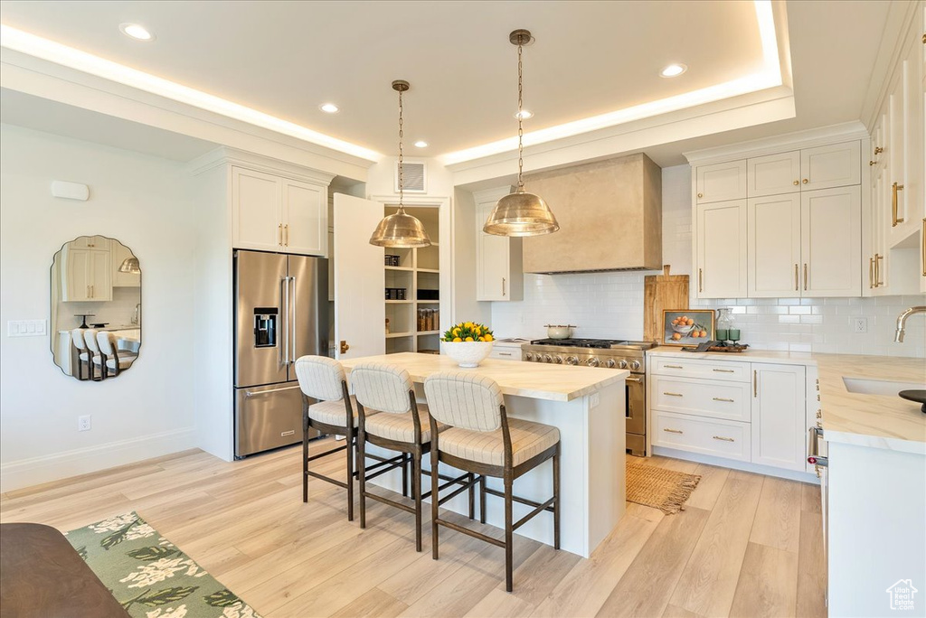 Kitchen featuring high quality appliances, custom exhaust hood, decorative backsplash, a kitchen island, and a kitchen bar