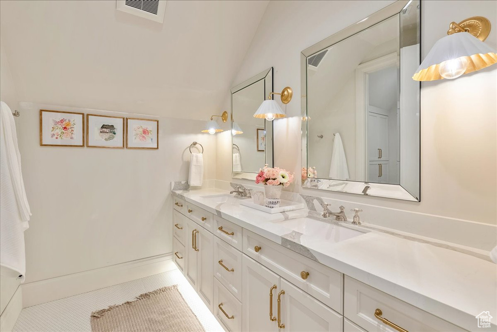 Full bath featuring double vanity, tile patterned floors, and vaulted ceiling