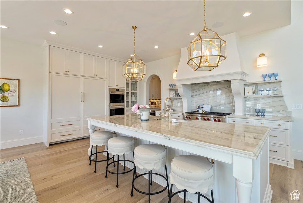 Kitchen with light wood finished floors, backsplash, arched walkways, a chandelier, and recessed lighting