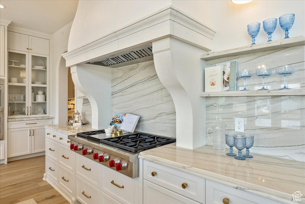 Kitchen with stainless steel gas cooktop, backsplash, light stone countertops, and white cabinets