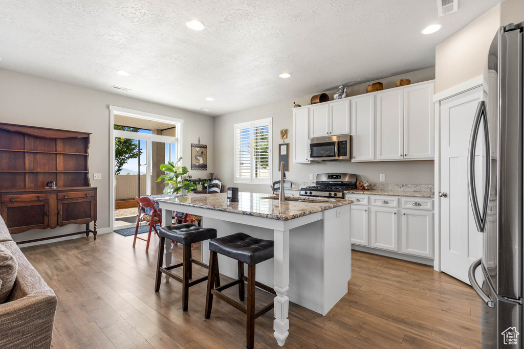 Kitchen with appliances with stainless steel finishes, white cabinetry, light stone countertops, wood finished floors, and recessed lighting