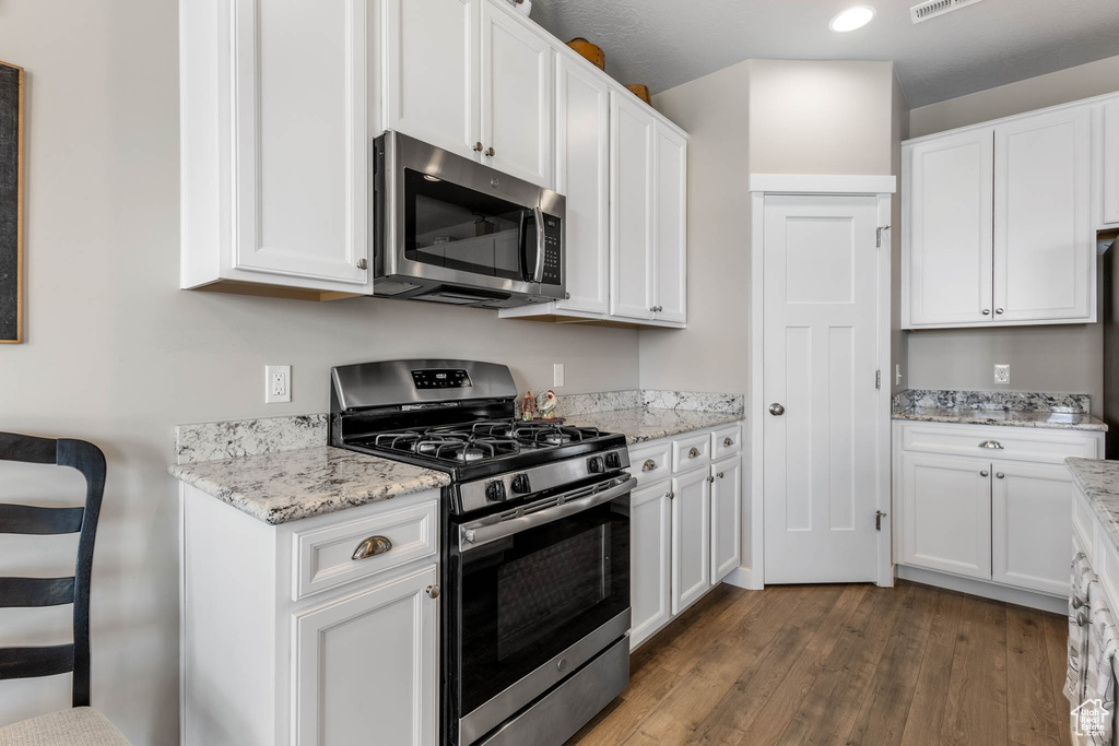 Kitchen featuring stainless steel appliances, dark wood-style flooring, white cabinetry, light stone countertops, and recessed lighting