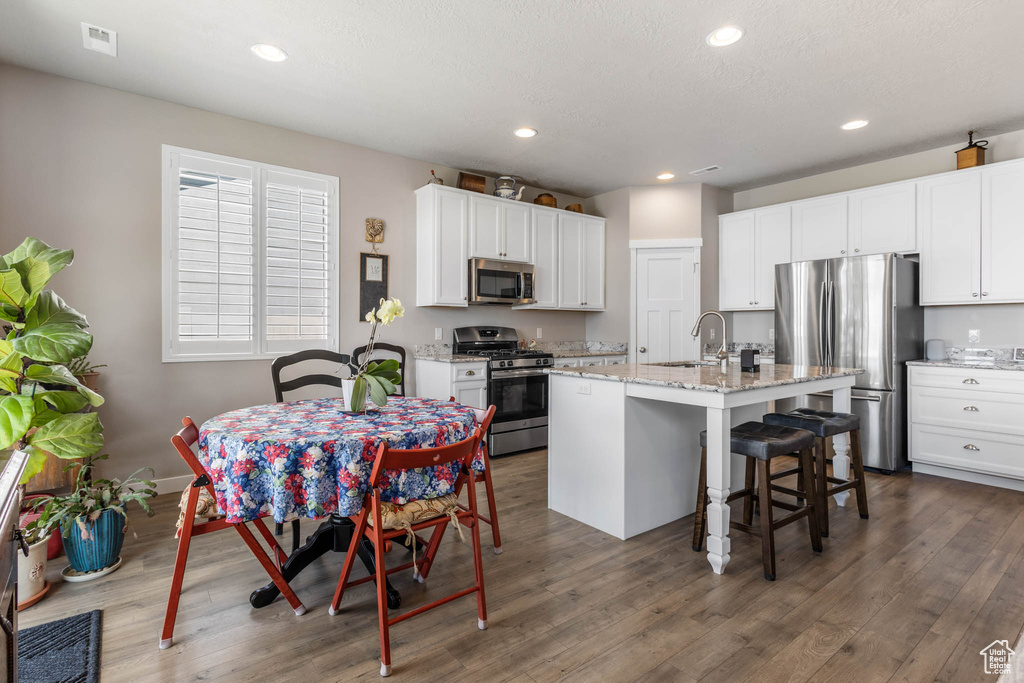 Kitchen with stainless steel appliances, white cabinetry, recessed lighting, a kitchen island with sink, and a kitchen bar