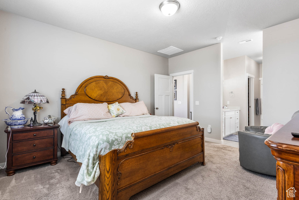 Bedroom with light colored carpet, ensuite bathroom, and baseboards